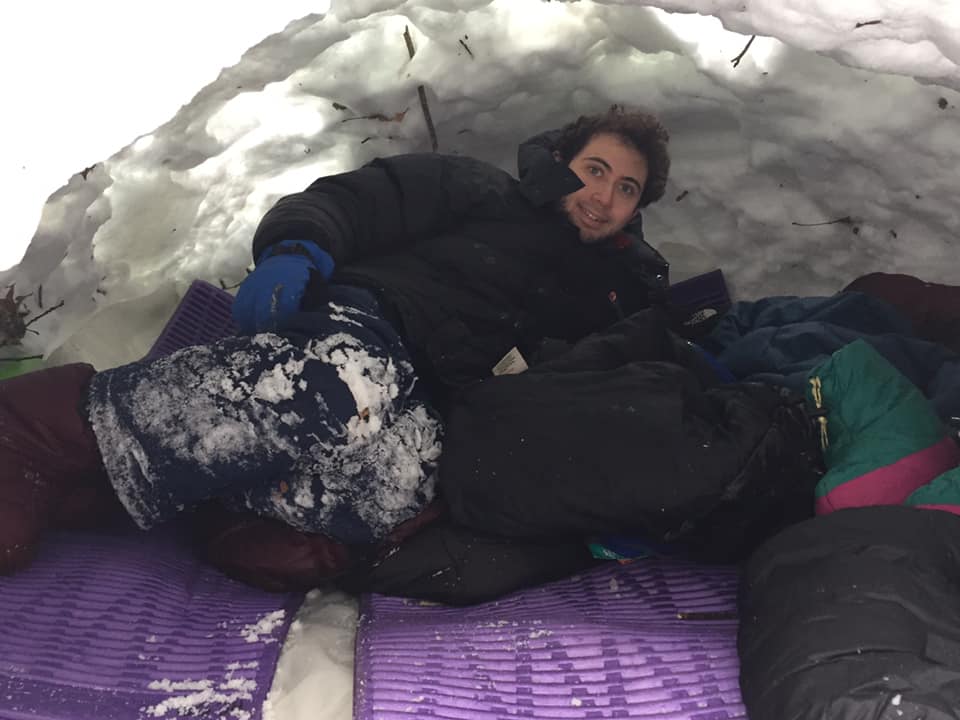 person in snow shelter for winter camping