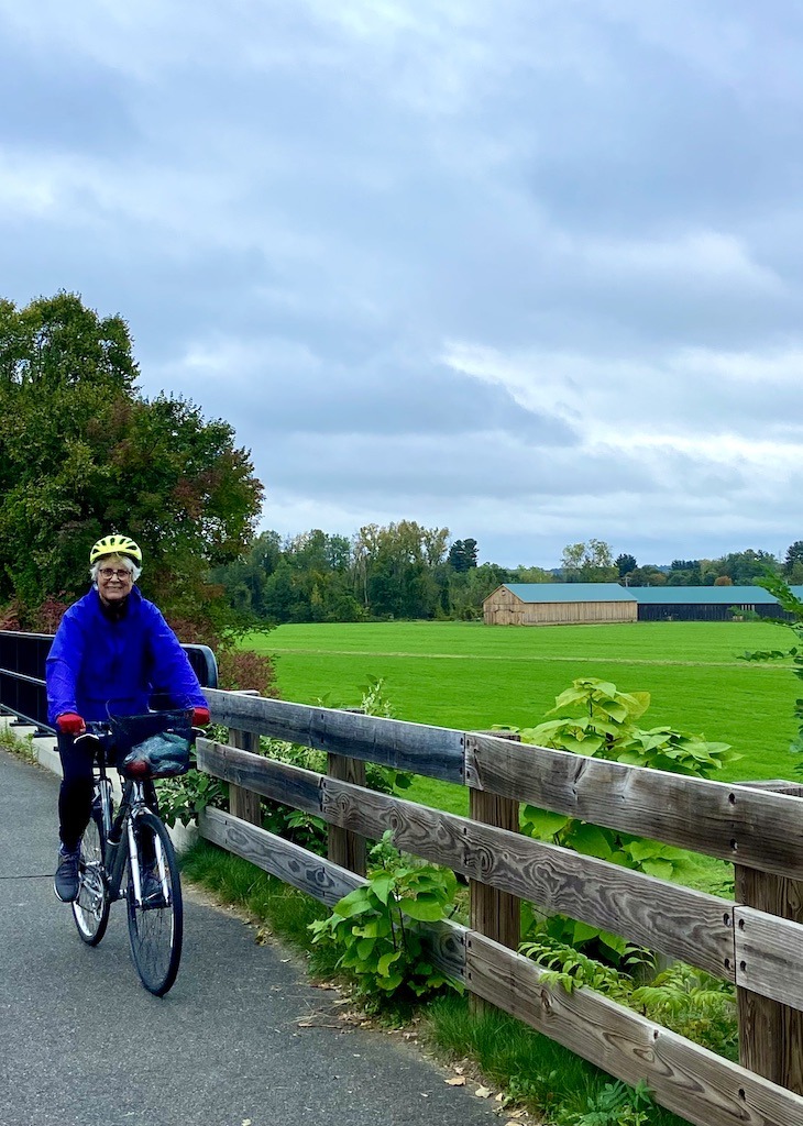 biker riding over bridge with tobacco barns in the background on one of the best bike trails in Western Massachusetts