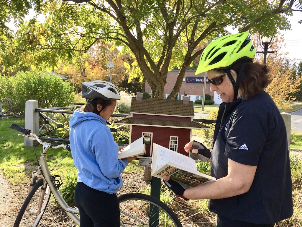 2 bike riders looking through books at a little library on one of the best bike trails in Western Massachusetts