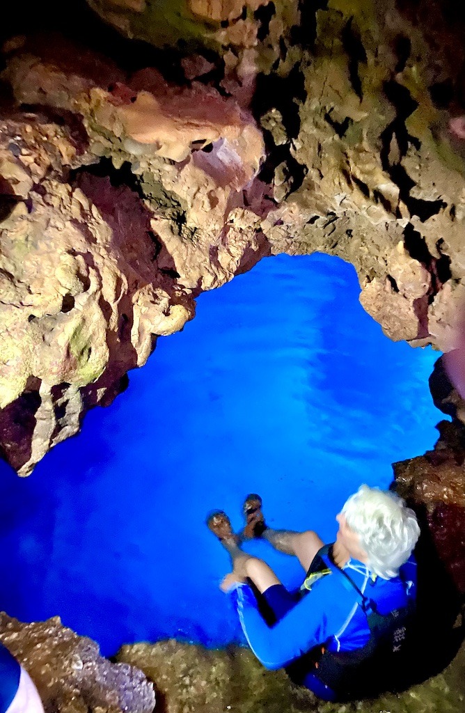 white haired person sitting near blue water of cave