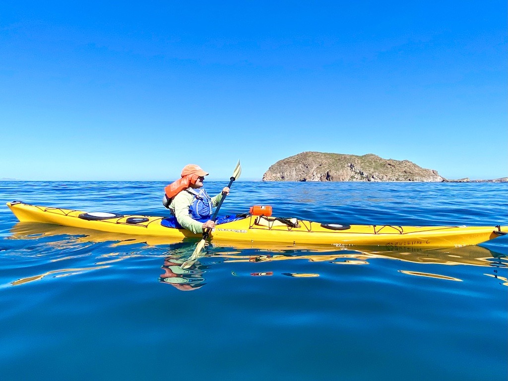 person with orange hat paddling a yellow kayak on blue water-Sea Kayaking in Baja