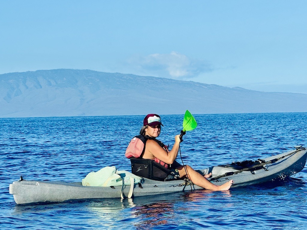 women in kayak on ocean with blue paddle