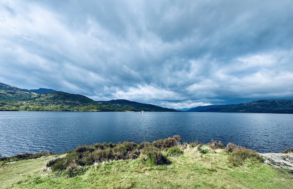 blue clouds over water with boat on the lake seen while E-biking Loch Katrine