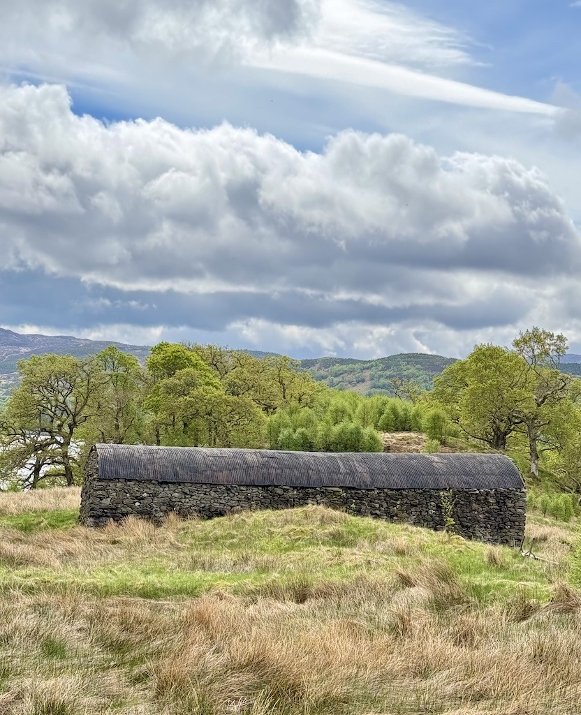 black stone house in a meadow with trees in the back seen while E-biking Loch Katrine