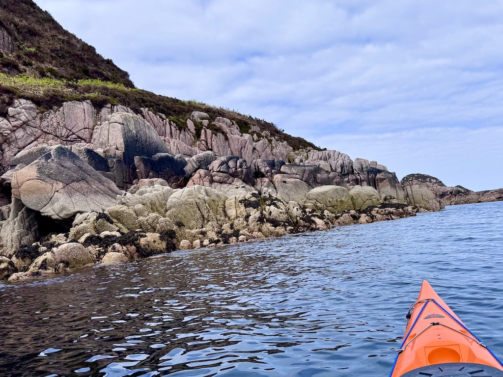 Tip of orange boat and pink granite cliffs while sea kayaking in Scotland