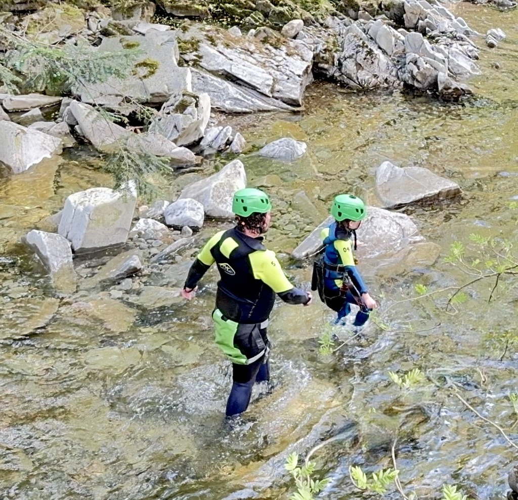 two people with green helmeits walking in a stream-outdoor adventure trip planning in Scotland
