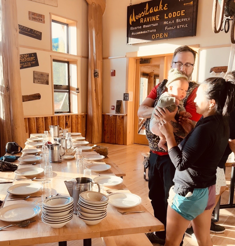 2 people holding a baby in dining hall of the Moosilauke Ravine Lodge 