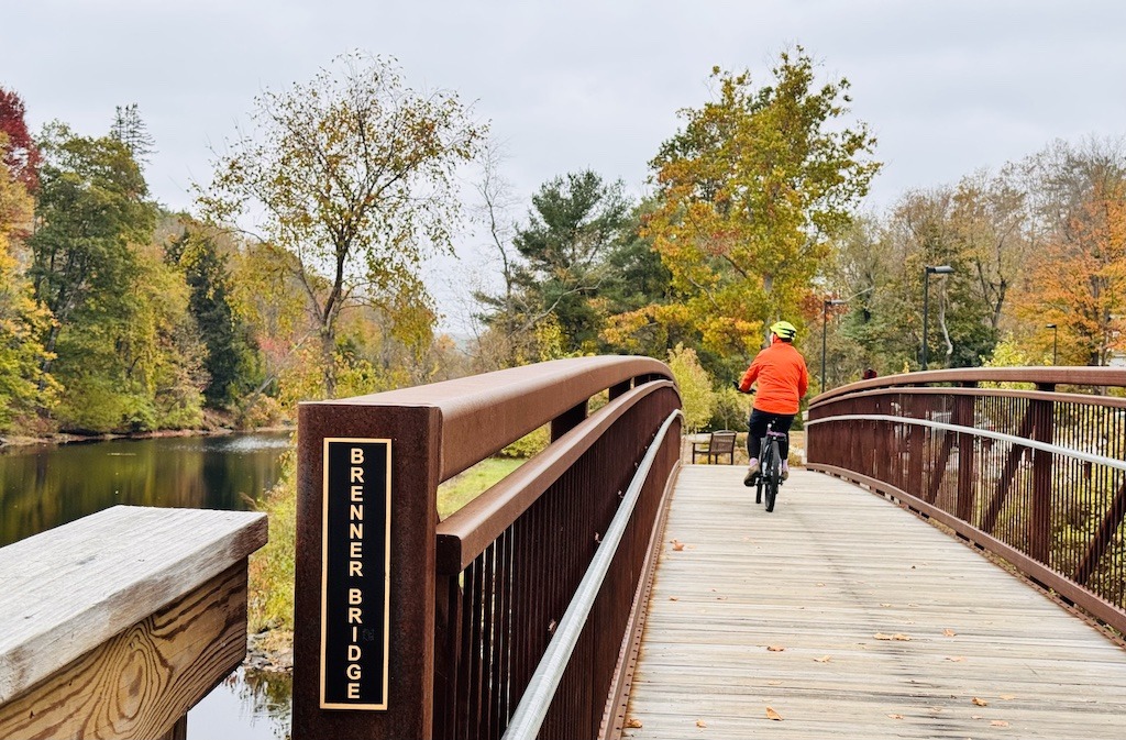 biker with orange coat crossing a bridge while biking in Southern New Hampshire
