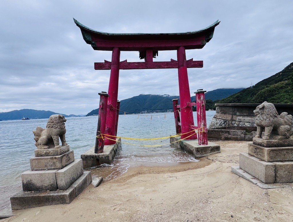 Red torii and lion statues near ocean while biking the Shimanami Kaido