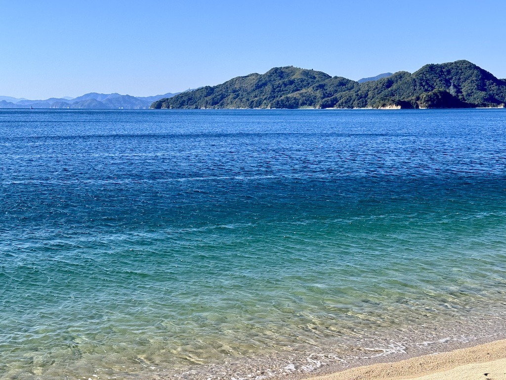 Blue green ocean water, beach, and mountains see while biking the Shimanami Kaido