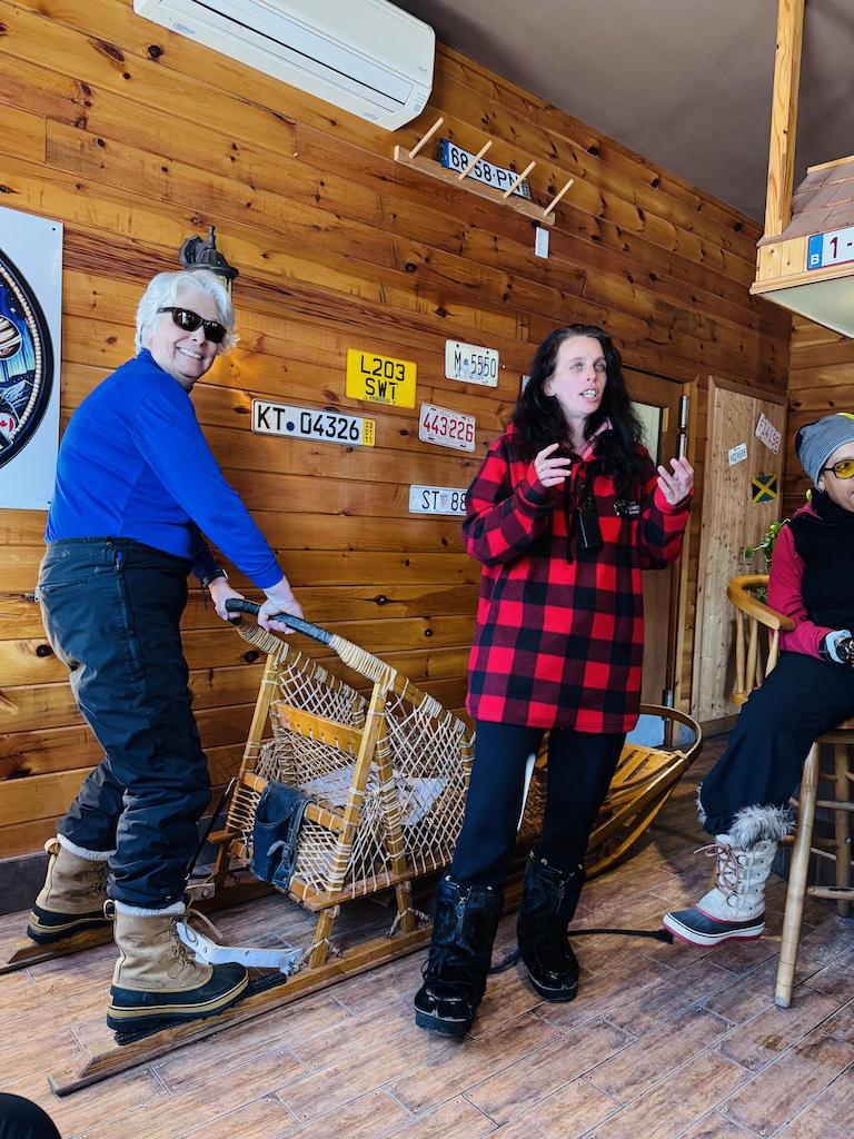 person in blue practicing on the dog sled while person in red instructs while Dogsledding in Quebec